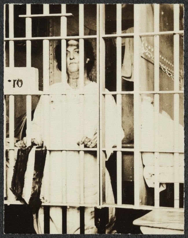 Woman standing behind bars of a prison cell.