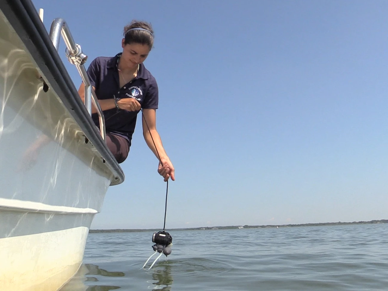 A woman leans over the edge of a boat with an underwater mapping tool. A woman leans over the edge of a boat with an underwater mapping tool.