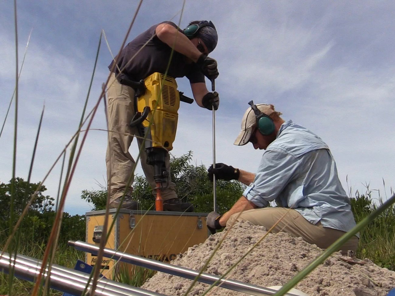 Two men use tools to install elevation markers in sandy soil. Two men use tools to install elevation markers in sandy soil.