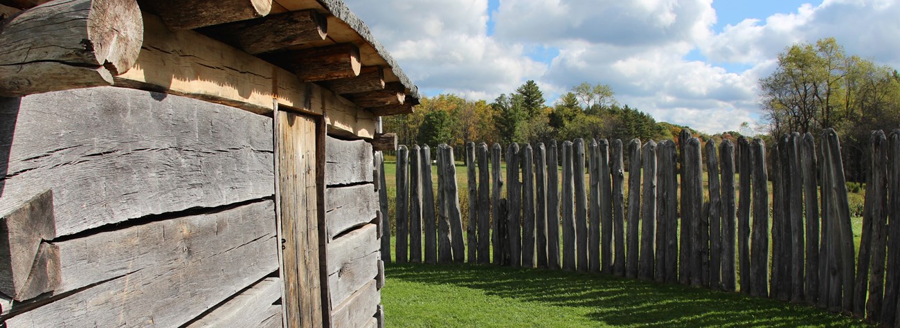 View of the side of a cabin and a post fence under a blue sky. View of the side of a cabin and a post fence under a blue sky.