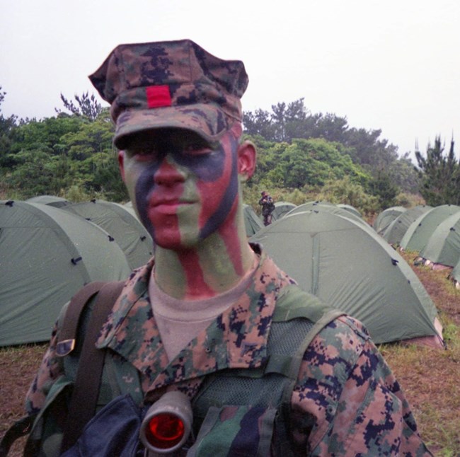 Kekoa Rosehill in a tent camp wearing camouflage face paint and military fatigues.