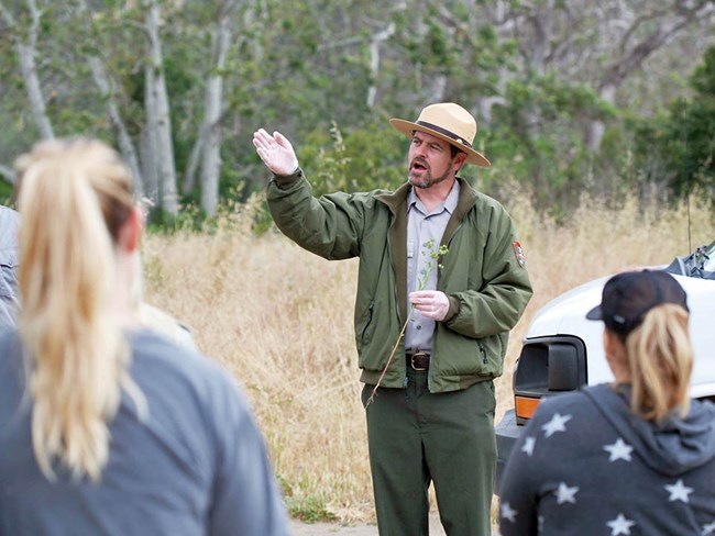 Joey Algiers holding a carnation spurge stem while speaking to volunteers