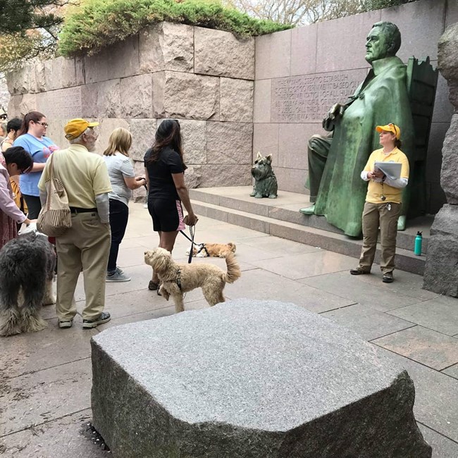Park volunteer talks to a group of people in front of sculpture of Franklin Delano Roosevelt.