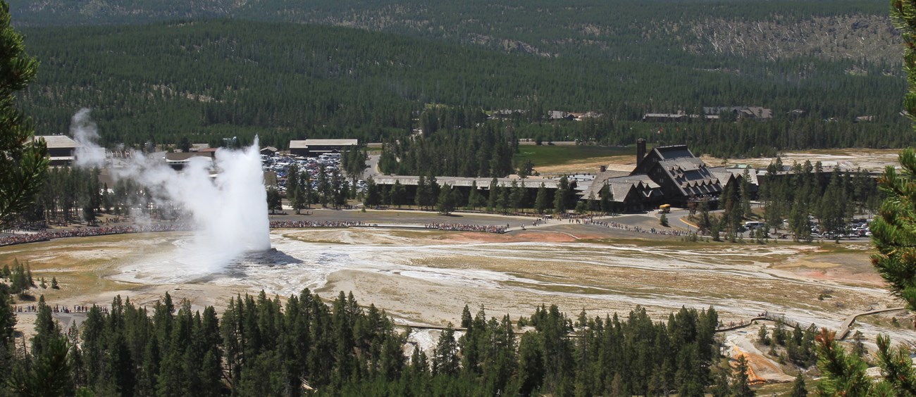 Steam and water shoots out of the top of a low, barren hill.