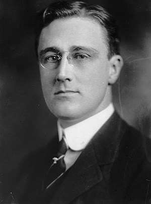 Black and white photo of a man wearing glasses and a suit with a tie.