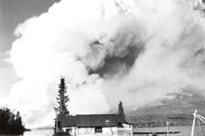 1953 Fire Behind Alsworth Home A black and white photograph of smoke from a wildfire behind a home