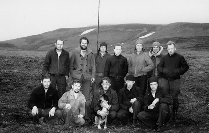 lt= Black and white photo of twelve men and a dog posing outdoors
