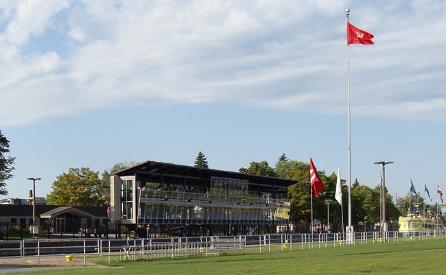 Two story black observation tower with a green grassy field in front and a building behind.