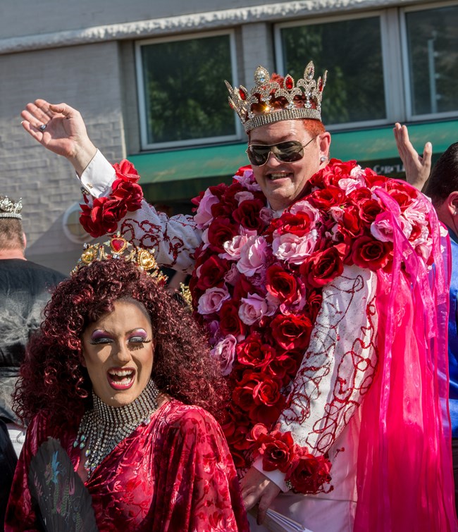 Two people in royal regalia wave to the crowd