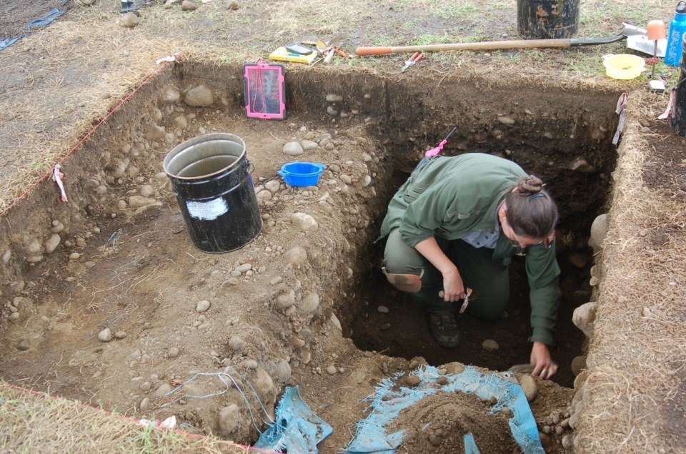 Archaeologist crouches in excavation unit.