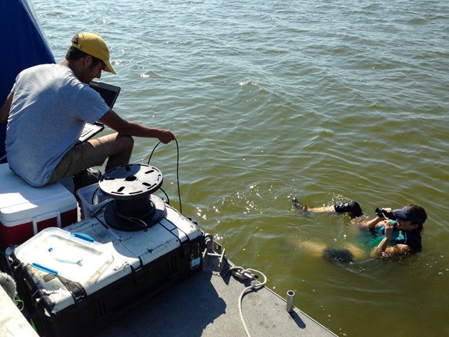 lt= a person floats in the water with camera equipment while a person deploys rope off a boat