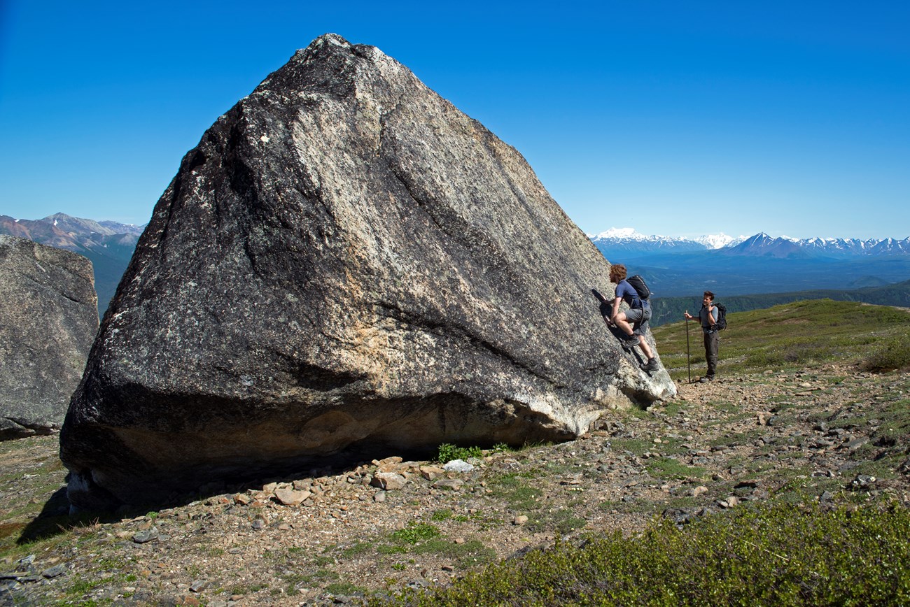 people standing next to an enormous, house-sized boulder