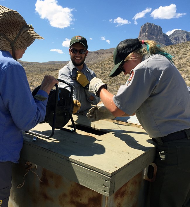 Three people lowering a cable into a well