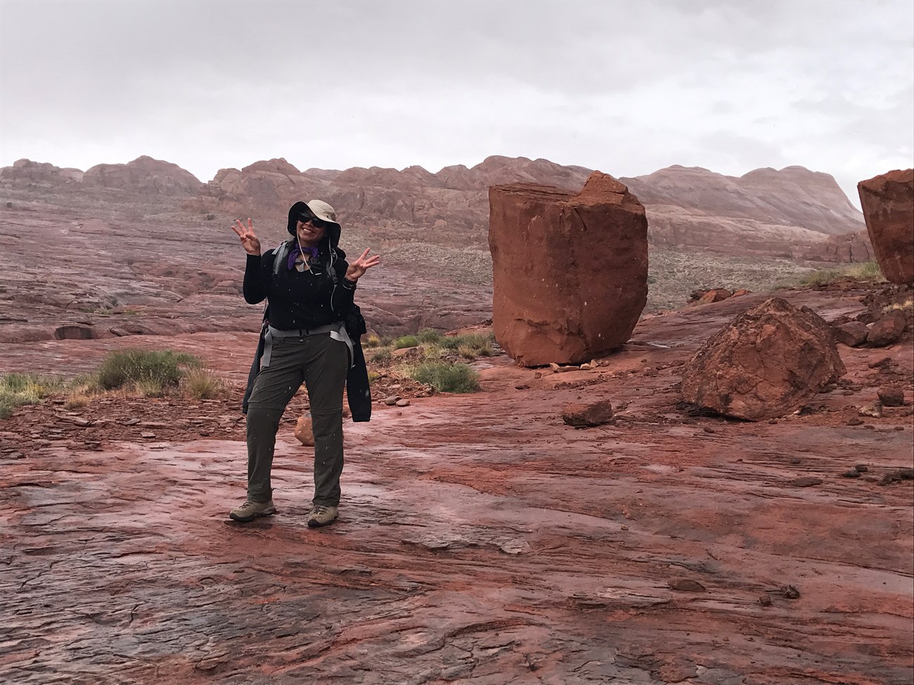 young woman in hiking clothing posing in front of reddish brown rocky landscape