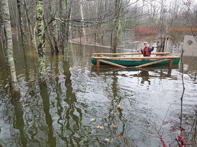person in a canoe floating on water flooded over a bridge and patio