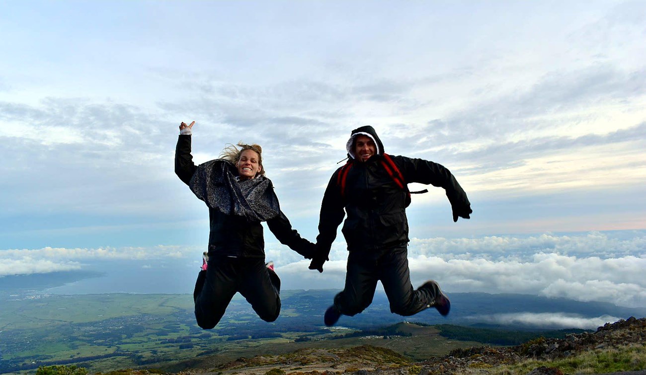 Two people jump with view of land and ocean behind them