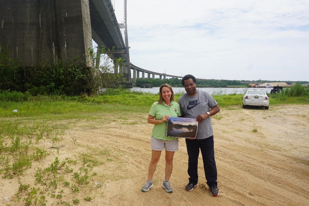 Smith-Incer and Womack hold the Mississippi State University concept plan under the Cochrane Africatown USA Bridge, where the Clotilda first landed. Photo by Margaret Gach, National Park Service.