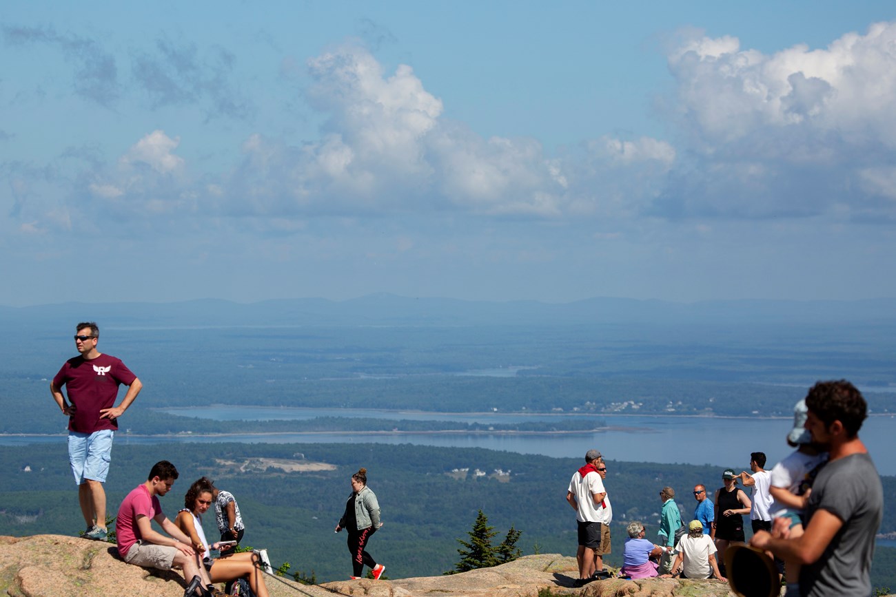 Busy Cadillac Summit visitors standing on granite ledge overlooking the ocean