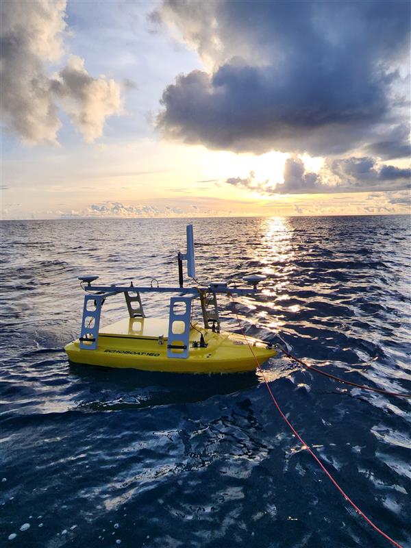 A small yellow boat floats in the ocean with the sunset in the background.