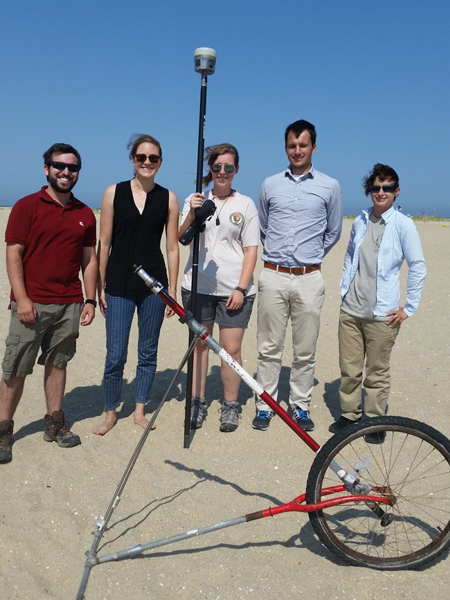 interns stand on a beach with tools used to measure shoreline change
