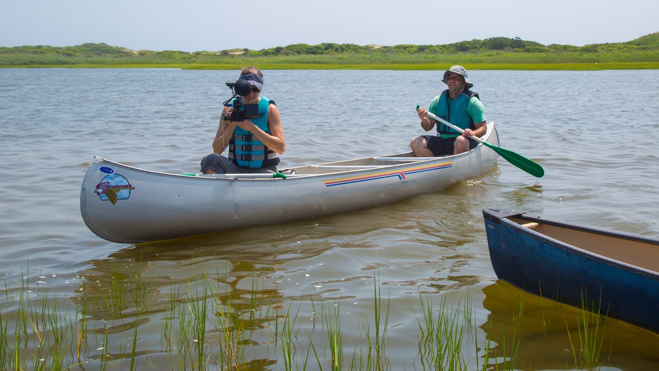 lt= two people sit in a canoe in a marsh with cameras