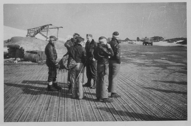 six men in bomber jackets standing on a fabricated runway