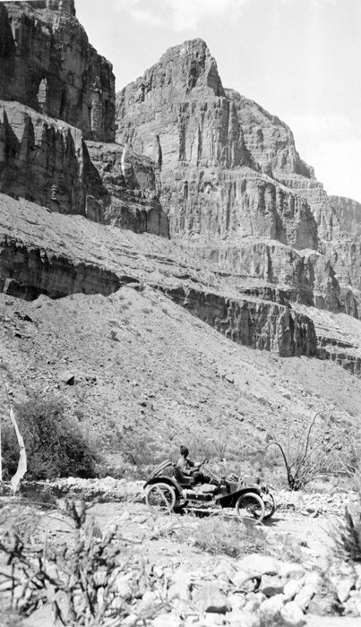 Metz drives along rugged terrain at the base of large canyon cliffs.