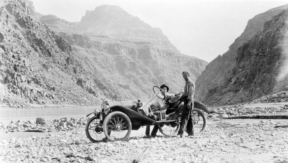 Car and its two drivers on a stretch of flat land inside of Grand Canyon.