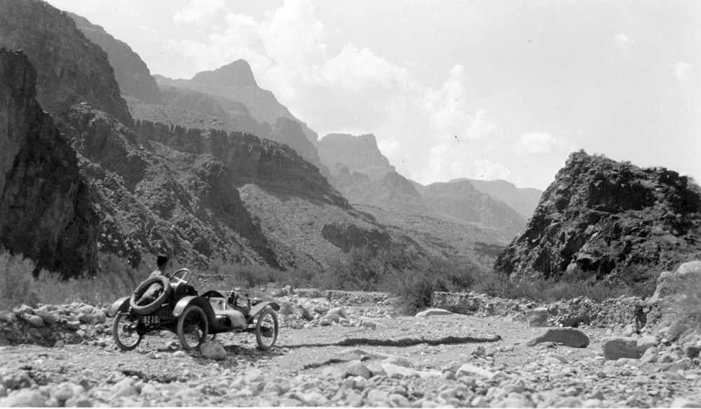 Old fashioned car faces a vast, rugged landscape.