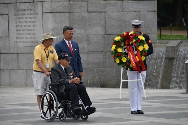 Volunteers help a veteran place a wreath at the World War II Memorial