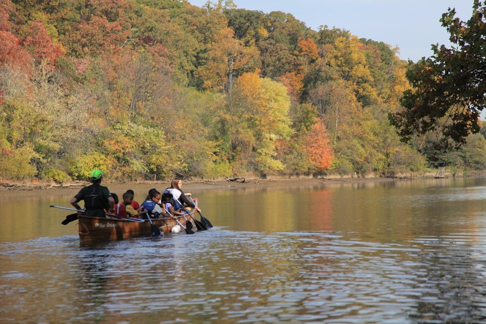 Young children in canoe paddling down calm river.
