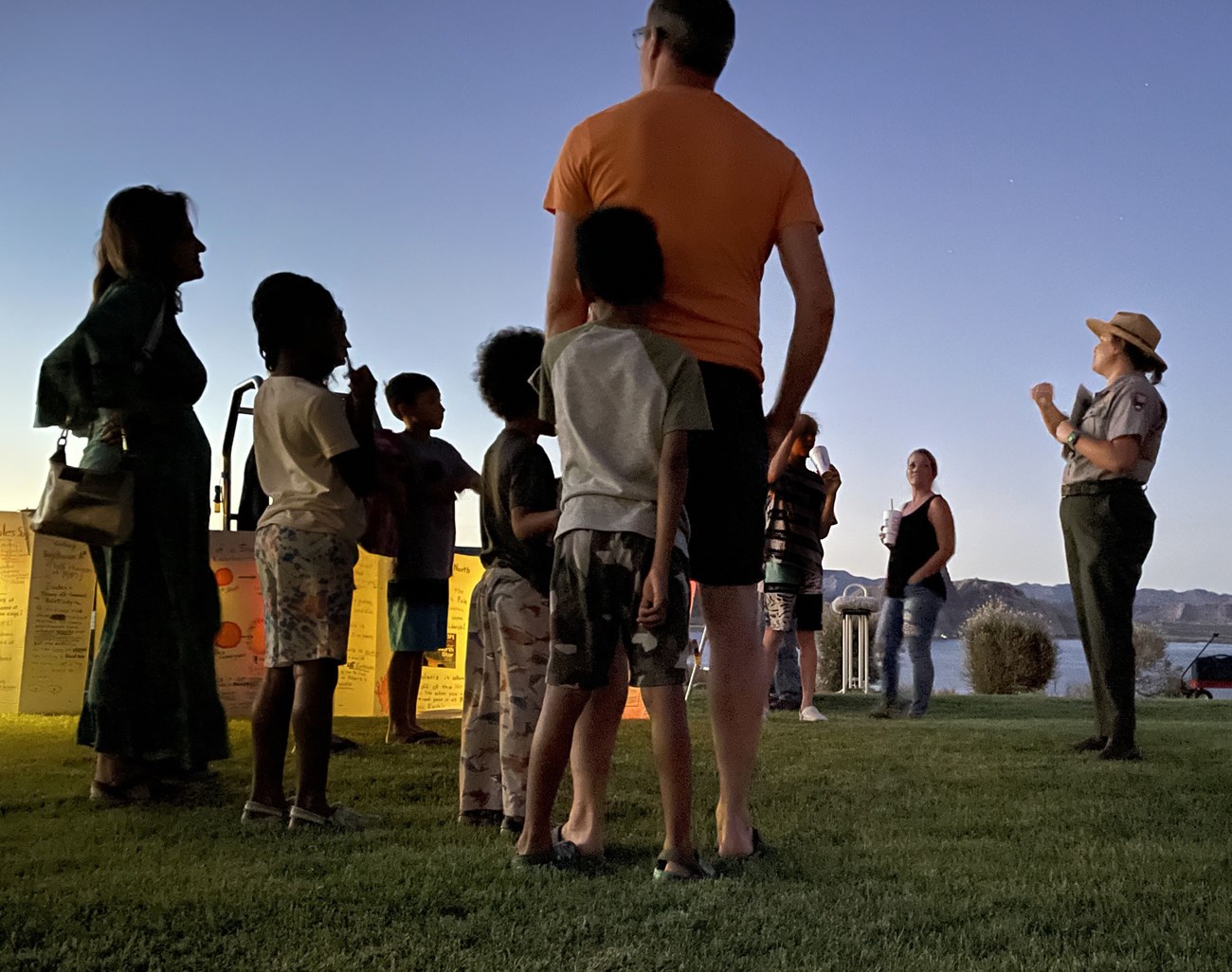 A park ranger talks to a crowd of people surrouding them at dusk.