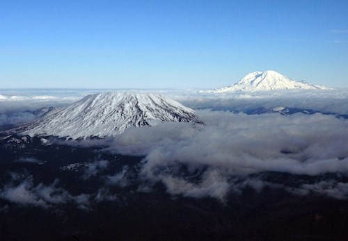 Two snowcapped volcanic peaks emerging above clouds.