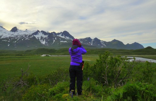 Joy scouting A woman looks out towards a green field and glacier