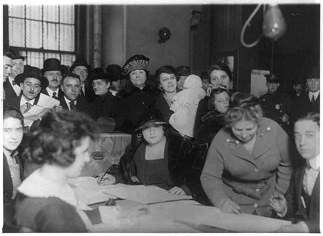 Women voting in 1922. Women wait in line to mark ballots as men watch.
