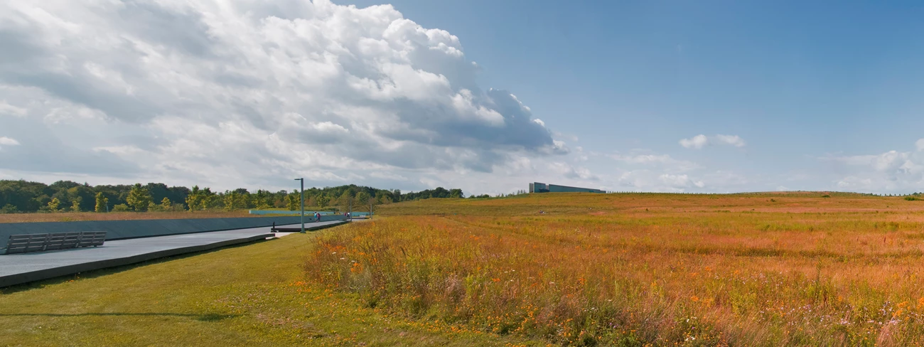 View of the memorial next to a large field of grasses and wildflowers under a blue sky. View of the memorial next to a large field of grasses and wildflowers under a blue sky.