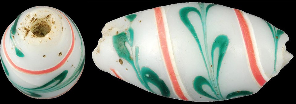 End and side views of a ellipsoidal bead, white with orange and white stripes and a green decoration spiraling around it from end to end.