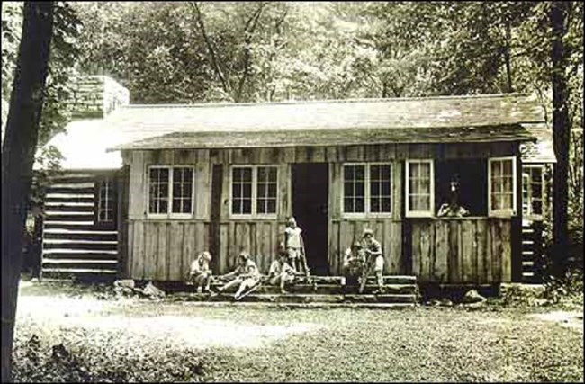 Children standing outside of a log structure. Children standing outside of a log structure.