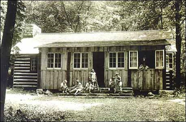 Children standing outside of a log structure.