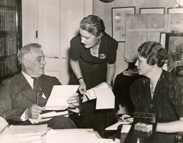 A man and two women work at a cluttered desk.