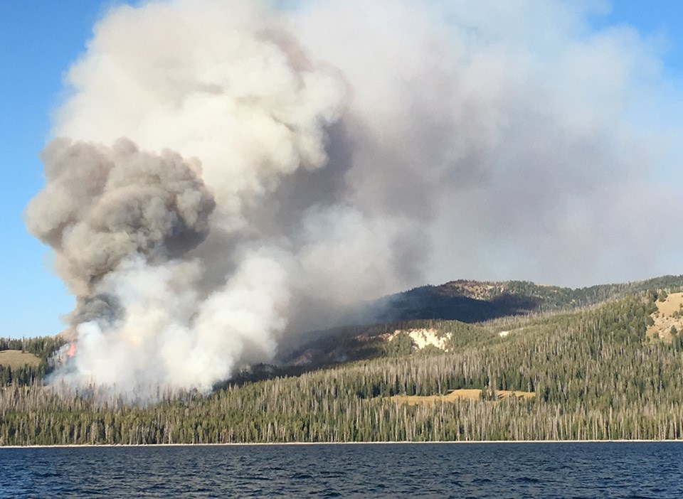 Brimstone Fire Smoke billows from a wildfire in mountainous terrain on the edge of a lake.