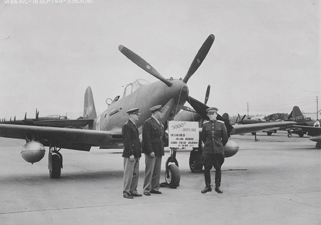 1940s photo of several men standing in front of an old plane.