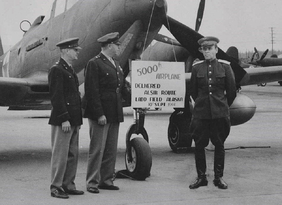 Close up of men standing in front of a plan with a sign that reads: "5000 airplane"
