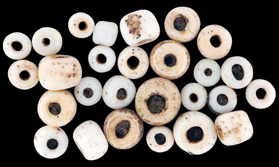 An assortment of spherical white beads, some with archaeological dirt in their center holes.