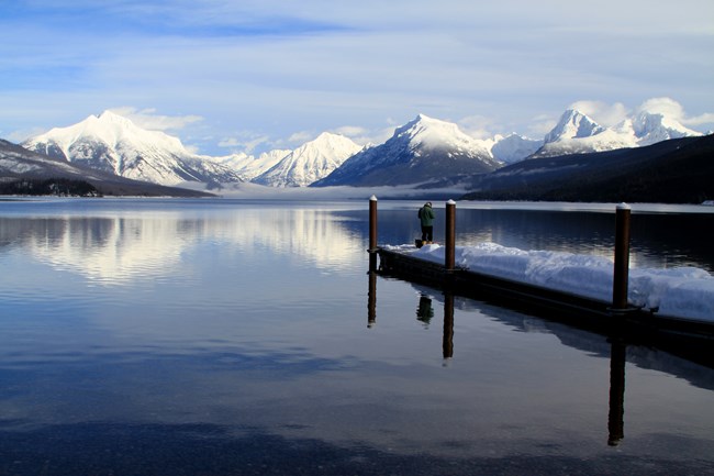 An angler stands on a snowy dock and puts a lure on his line.