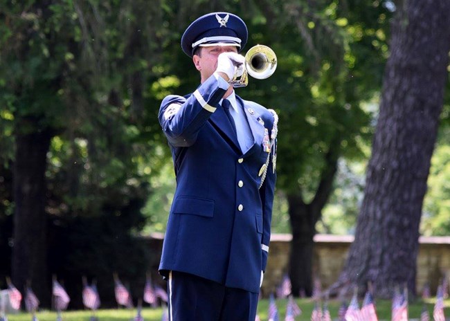 man in military uniform preforms Taps on a bugle