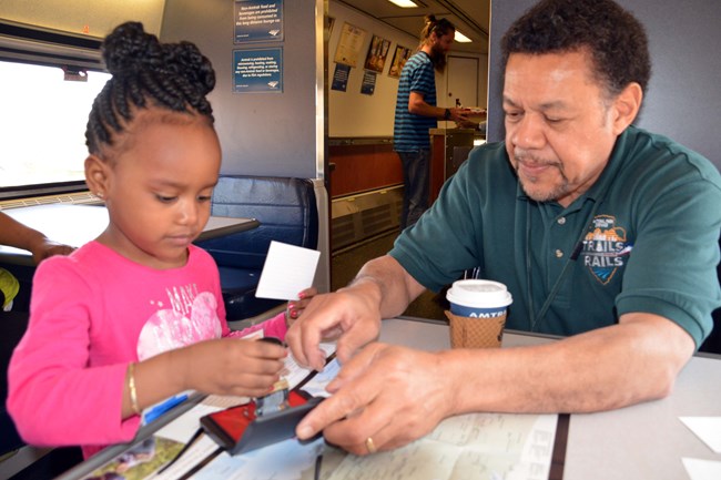 Volunteer helps young girl put passport stamp on a piece of paper