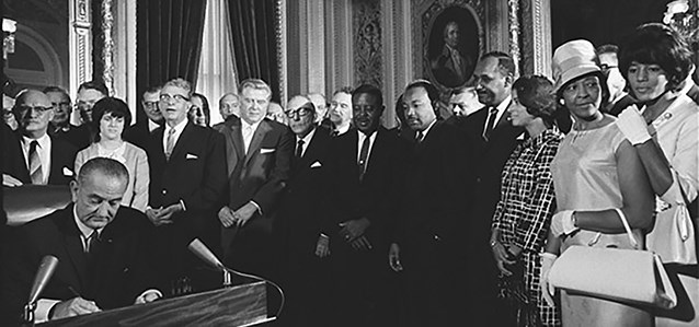 large crowd watching a man sign a paper at a desk