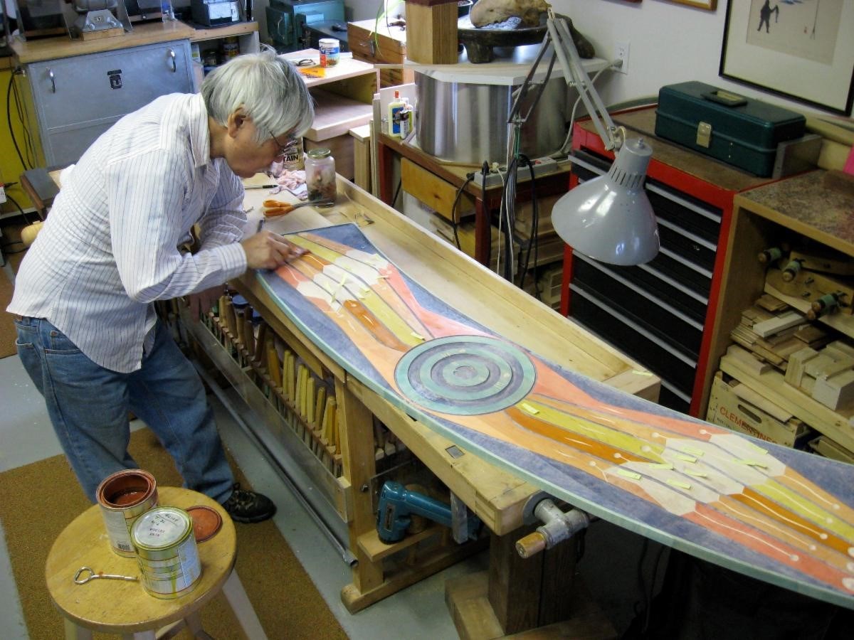 alaska native artist in a workshop, painting a large wooden piece of art