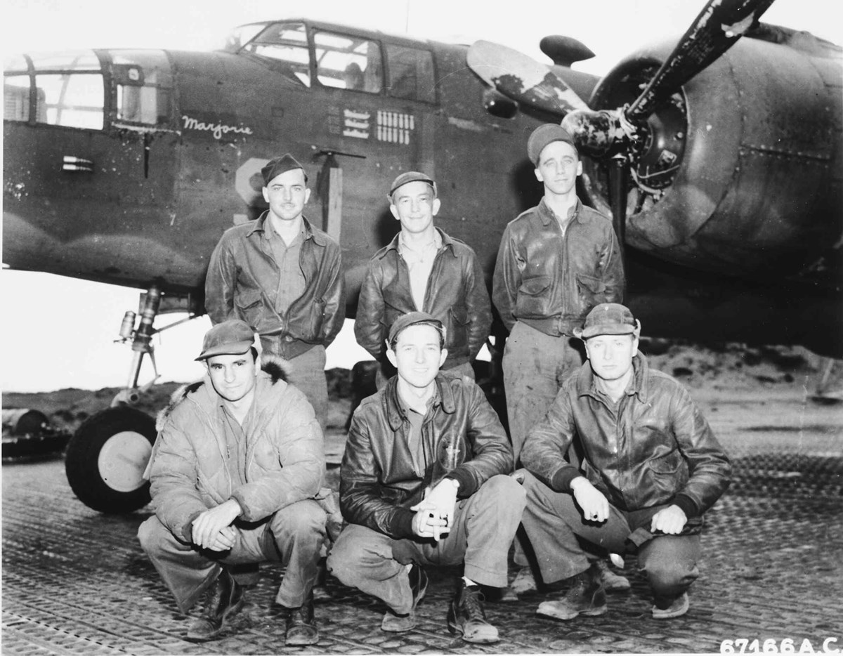 two rows of men pose in front of an airplane